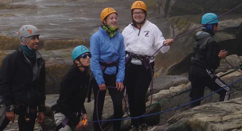 A group of people wearing safety gear stand near a large rock. 